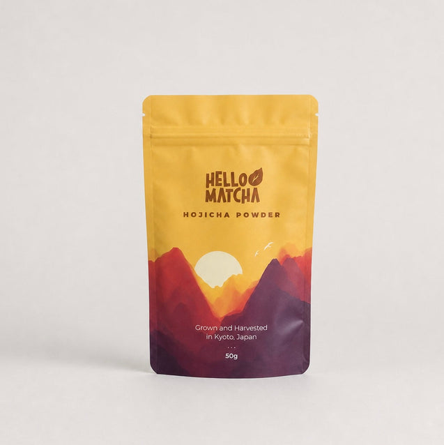 A 50g stand-up pouch of Hello Matcha Hojicha Powder, featuring a yellow-to-purple mountain sunset design on a light gray background.