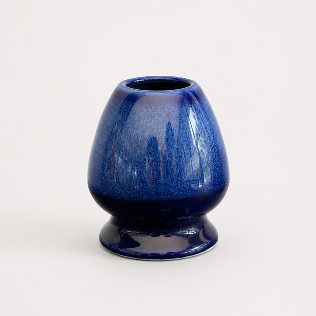 A small glossy ceramic vase with a rounded bulbous body and short pedestal base, glazed in deep cobalt blue with darker mottled shading, photographed on a clean white background.